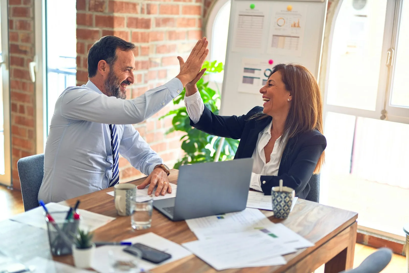 Two colleagues high-fiving at a desk after closing a deal