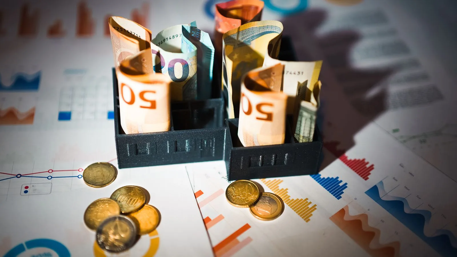 A close-up of euro banknotes and coins on top of financial charts symbolizing investment and economic analysis.