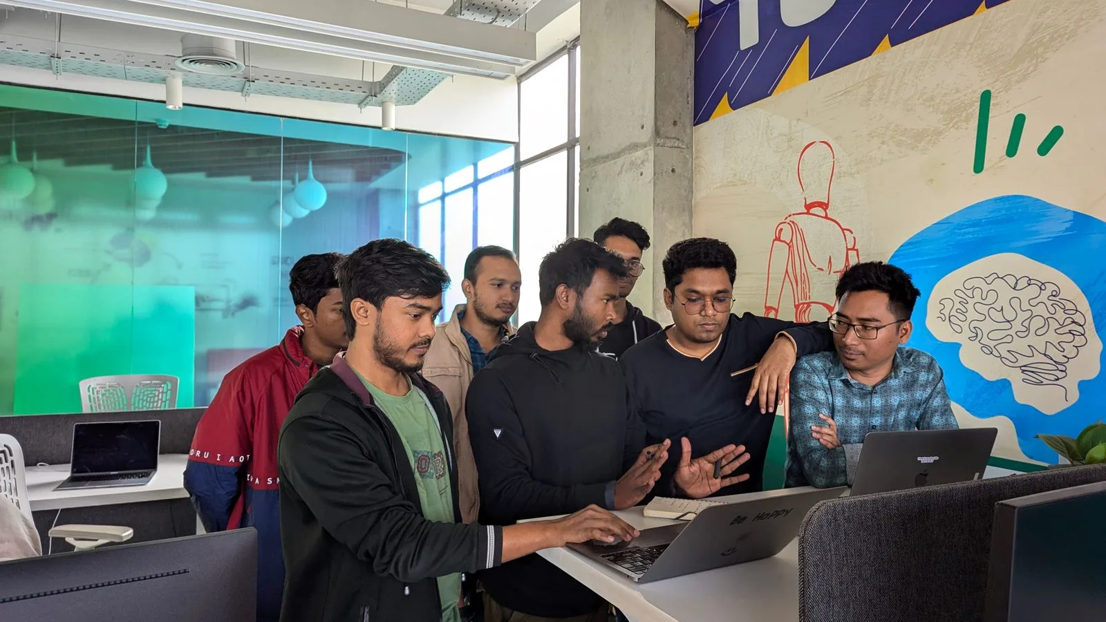 Young professionals collaborate around a laptop in a vibrant, modern office environment.