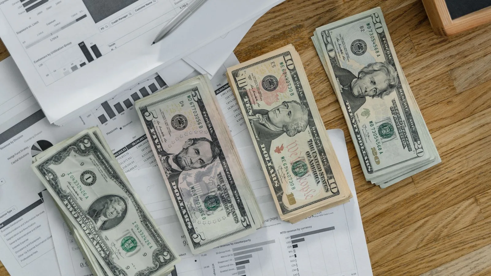 Stacks of US Dollar banknotes placed over financial documents and reports on a desk.