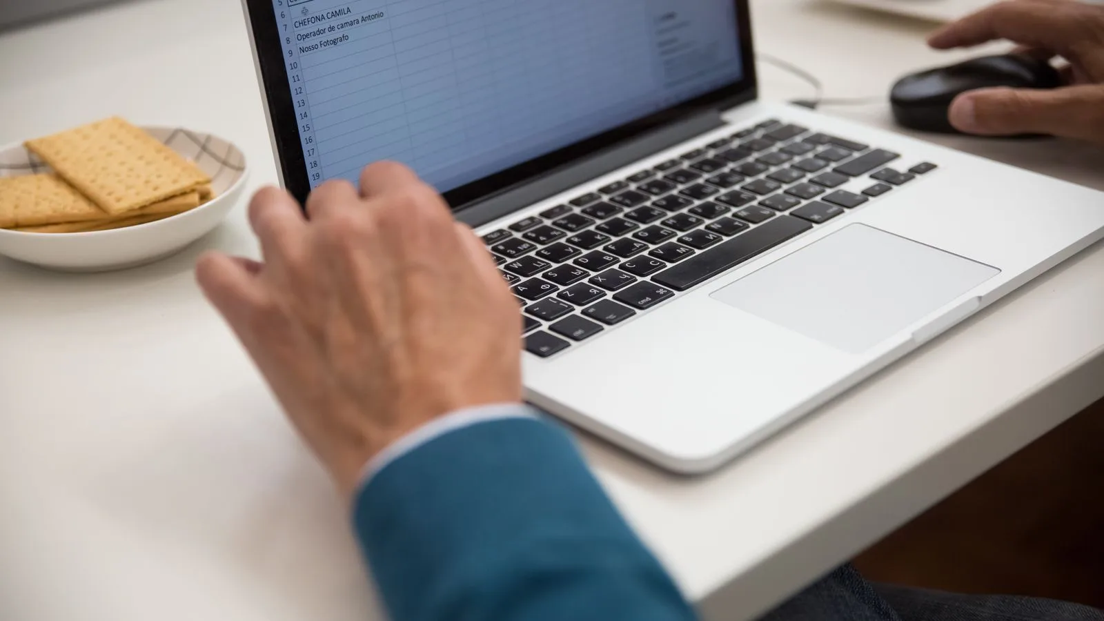 A person working on a laptop at a desk with snacks, emphasizing productivity and technology.