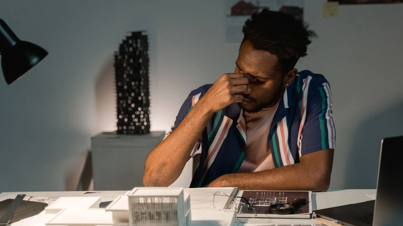 Tired architect working at night on architectural models and design plans.