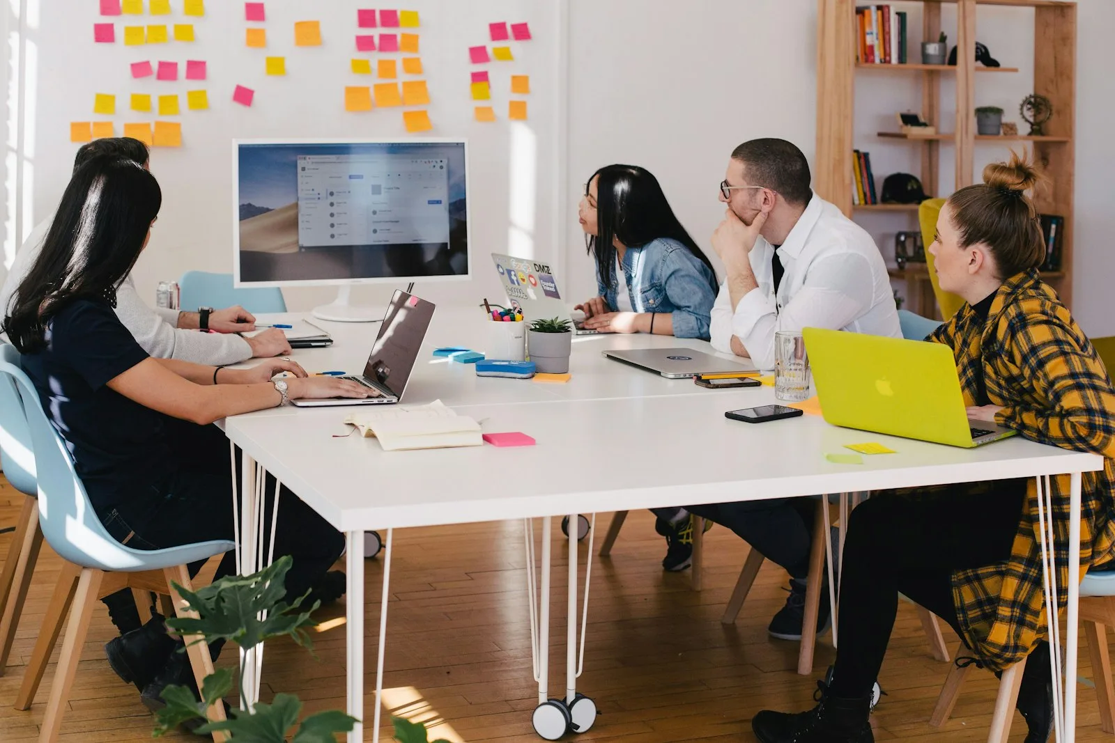 A team meeting in front of a wall covered in colorful sticky notes