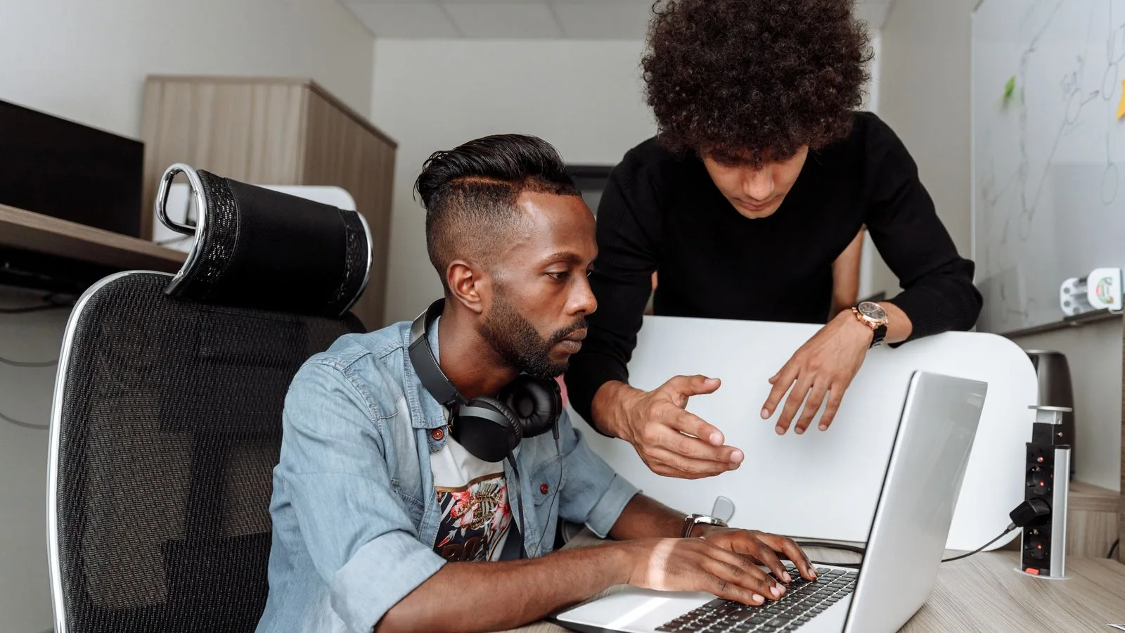 Two diverse male colleagues collaborating on a laptop in a modern office environment.