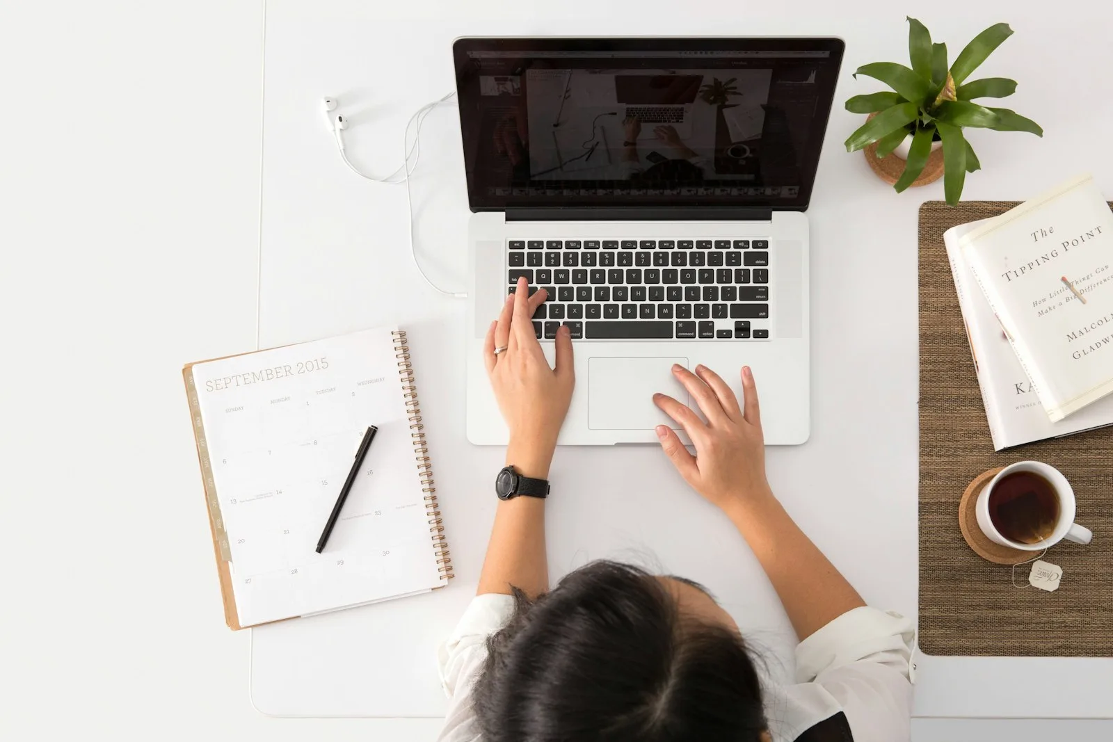 Overhead view of someone typing on a laptop beside a planner and coffee