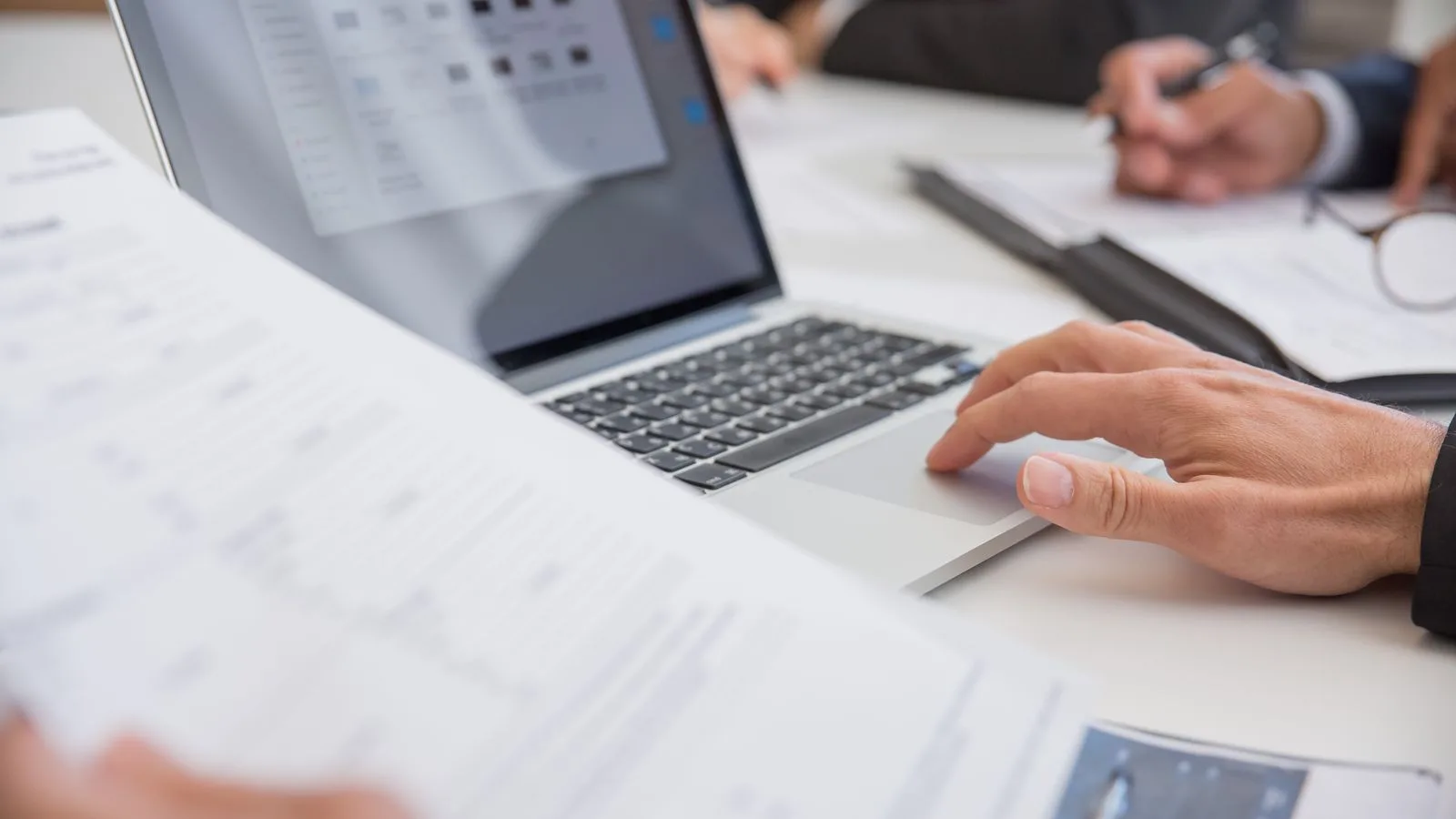 Close-up of hands working on documents and a laptop in an office setting, illustrating teamwork and productivity.