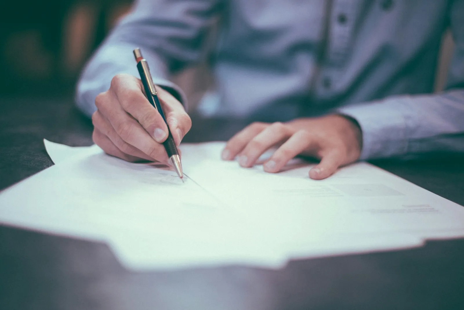 A hand signing a document with a pen at a desk