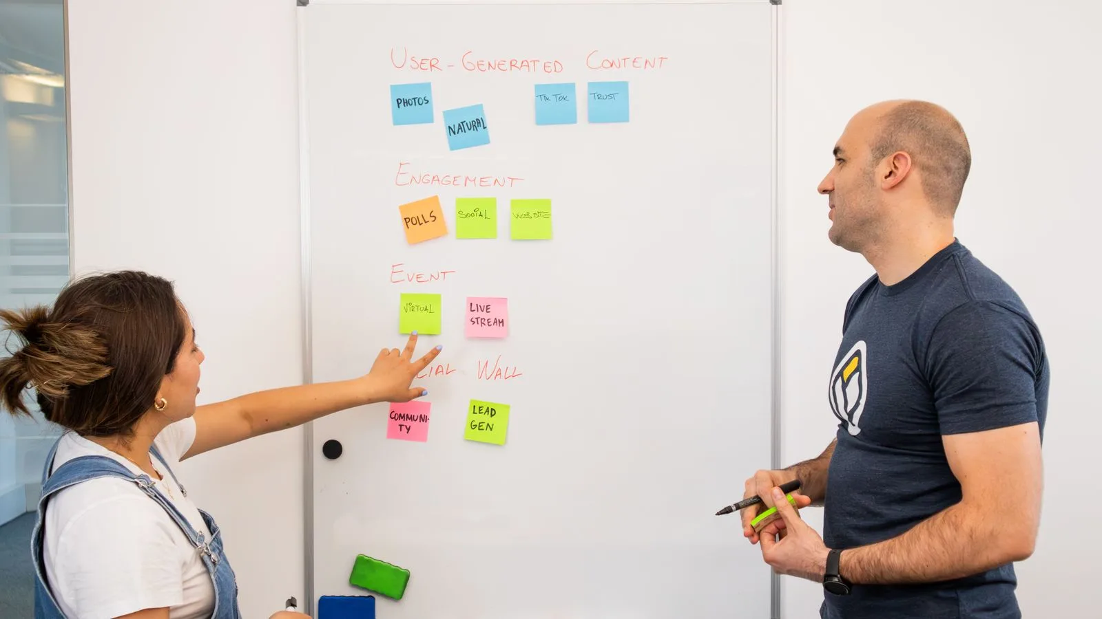 Two professionals brainstorming and planning projects on a whiteboard in a collaborative office setting.