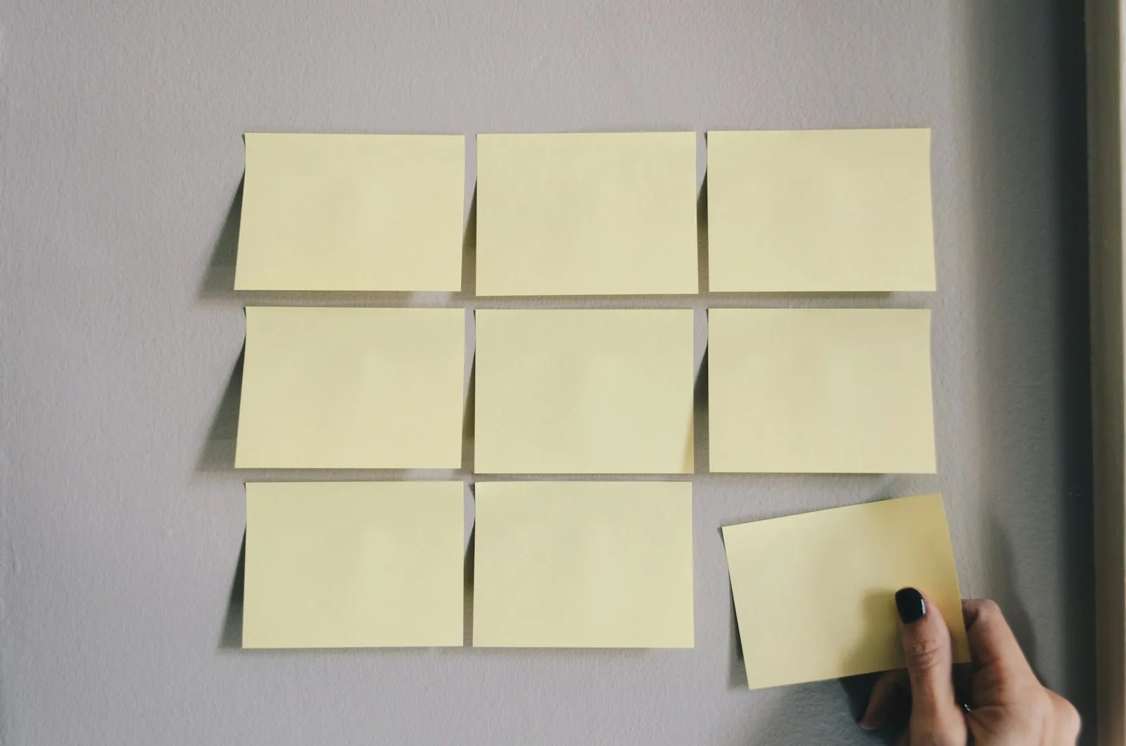A hand placing a sticky note on a wall of yellow sticky notes