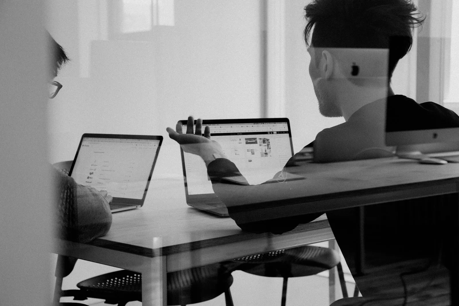 Two colleagues reviewing work on laptops at a desk