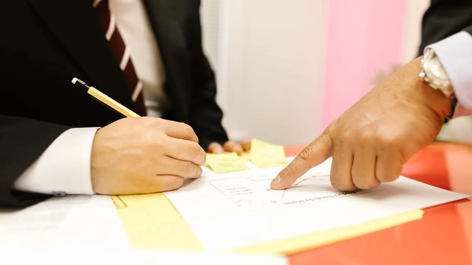 Close-up of two professionals in a meeting, reviewing documents with a pen and paper.